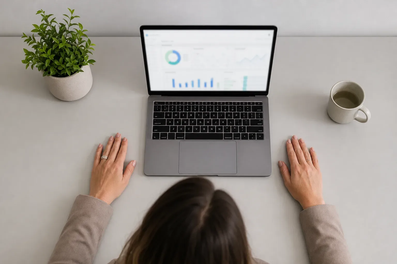 A half-open laptop with a blurred analytics interface glowing on its screen on a clear work surface, seen from above in bright flat light, a paralegal's hands placed flat on the desk surface beside the laptop rather than on the keyboard, the screen showing abstract intake metric panels with lead-to-consultation and response-time groupings, all content unreadable.