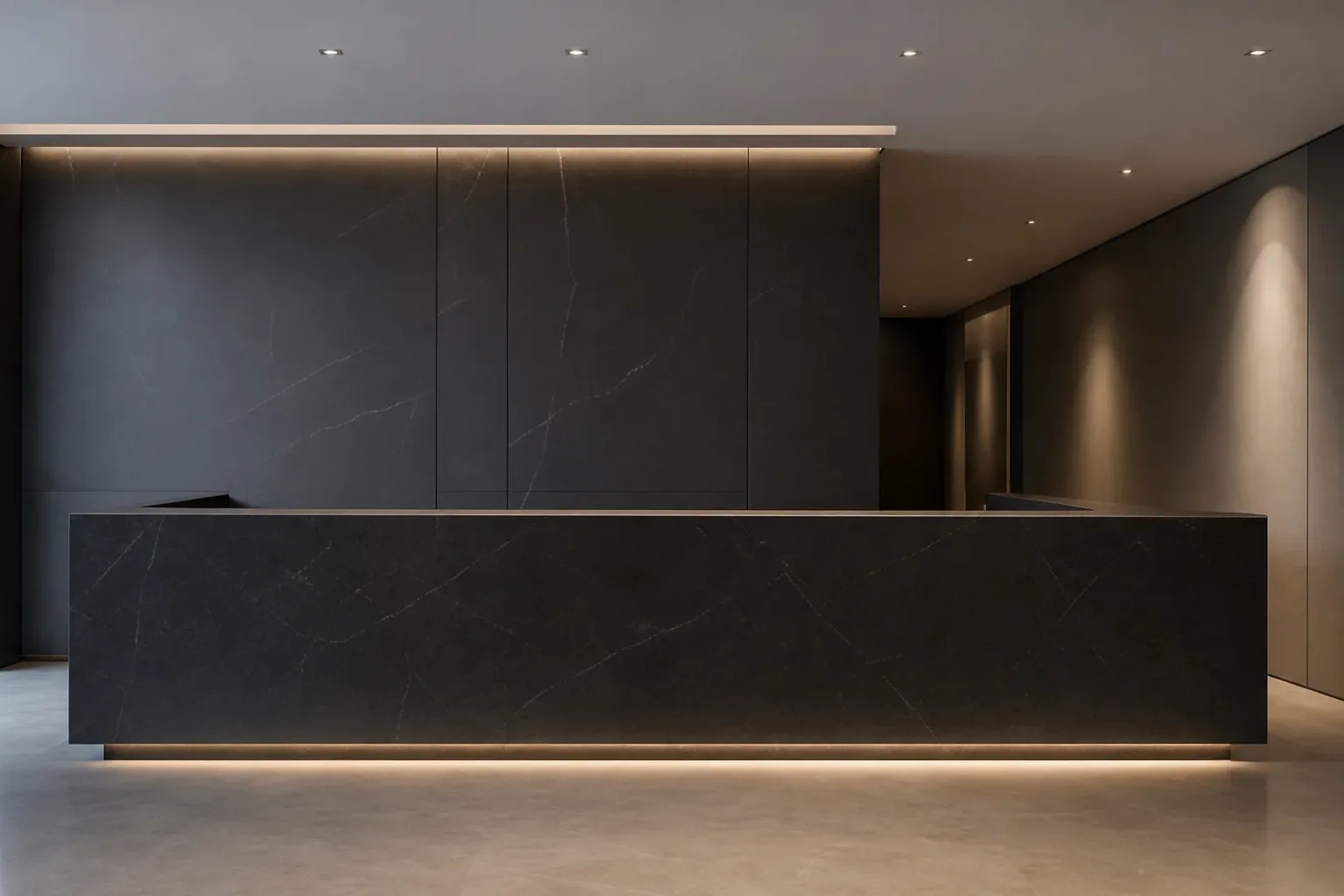 A sleek law firm reception counter in dark stone extending across the frame in a wide view lit by cool ambient light from above, no person behind it, the orchid absent and the stone surface entirely unoccupied, the corridor behind the counter receding into shadow.