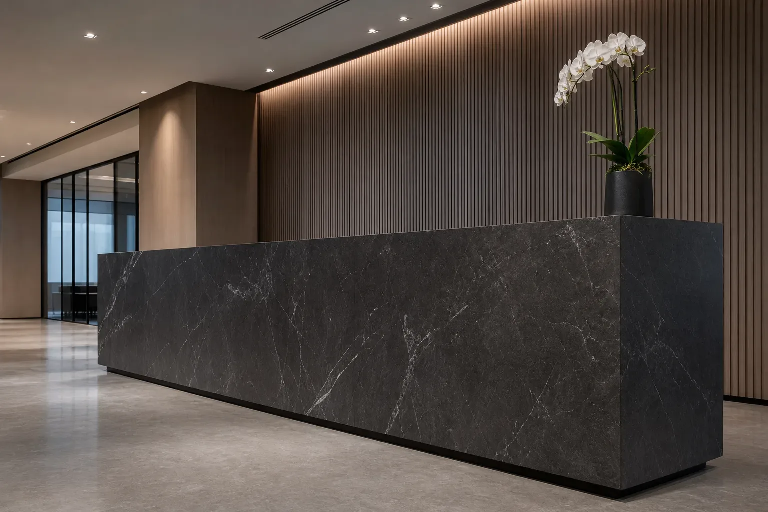 A sleek law firm reception counter in dark stone, shot from a low angle looking upward in calm even daylight, a single orchid at one end of the counter, nobody behind it, the stone surface bare.