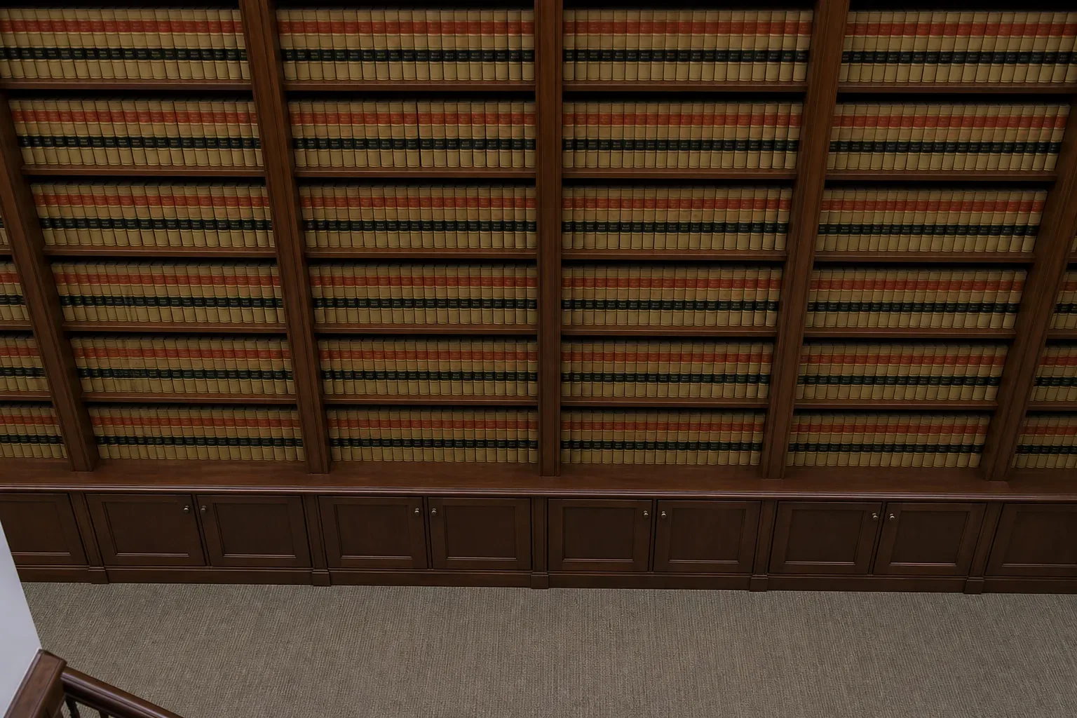 A floor-to-ceiling shelf of uniform bound law reports in a firm library, seen from above in bright flat light, no person present, a low timber credenza visible at the base of the shelving unit, the spines of the volumes filling the background from floor to ceiling.