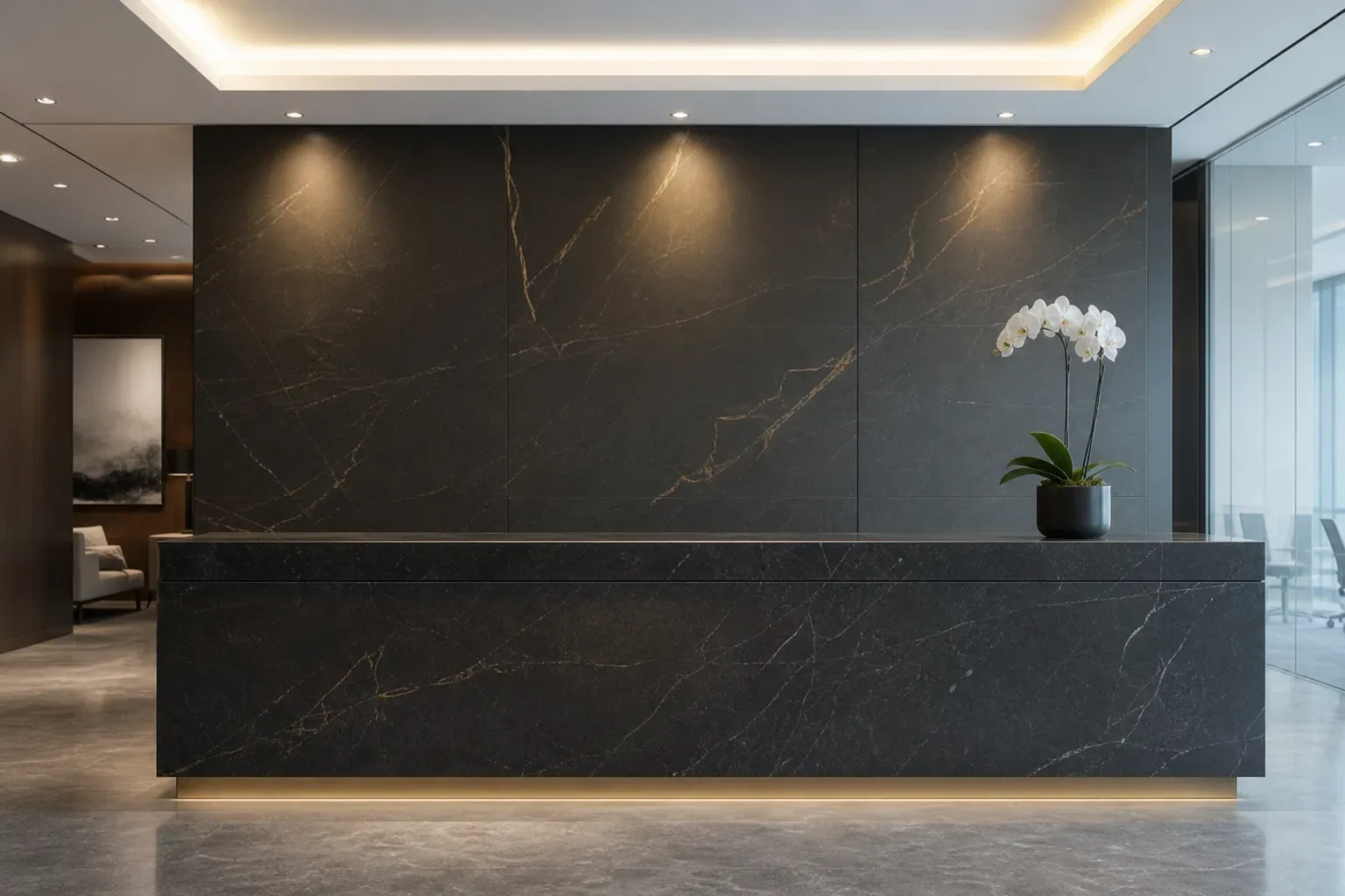 A sleek law firm reception counter in dark stone, a wide view with cool ambient light from above, nobody behind the counter, a single orchid at one end and the stone surface otherwise unoccupied.