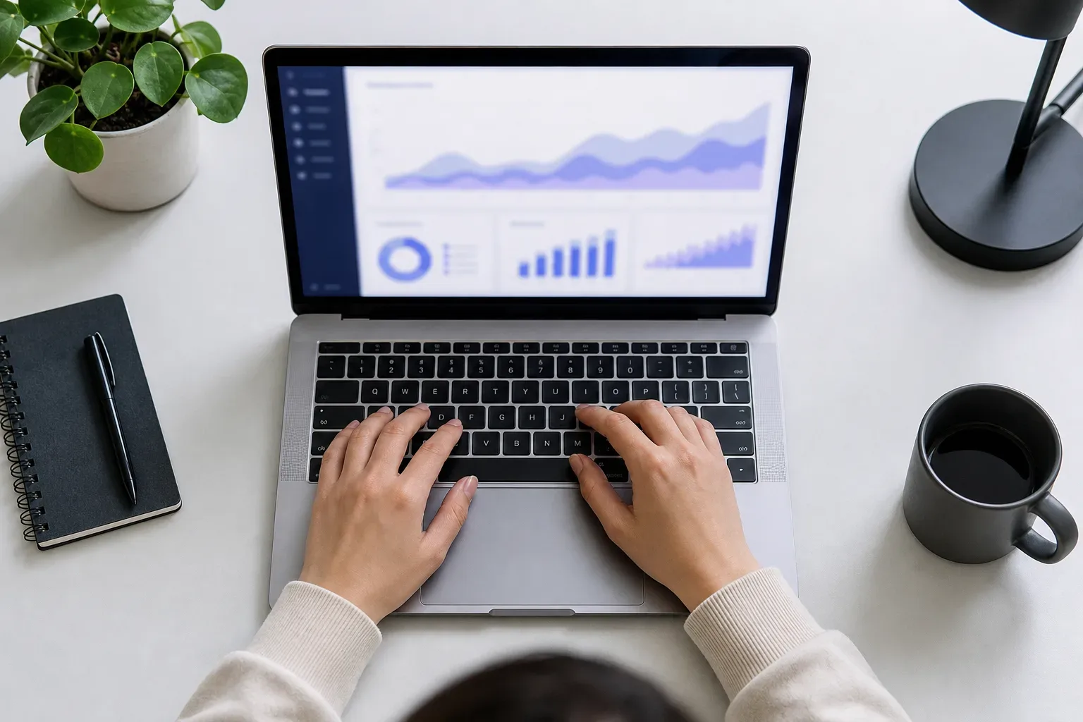 A half-open laptop with a blurred analytics interface glowing on its screen on a clear work surface, seen from above in bright flat light, a digital marketing strategist's hands on the keyboard below the screen, the screen showing abstract organic traffic growth panels.